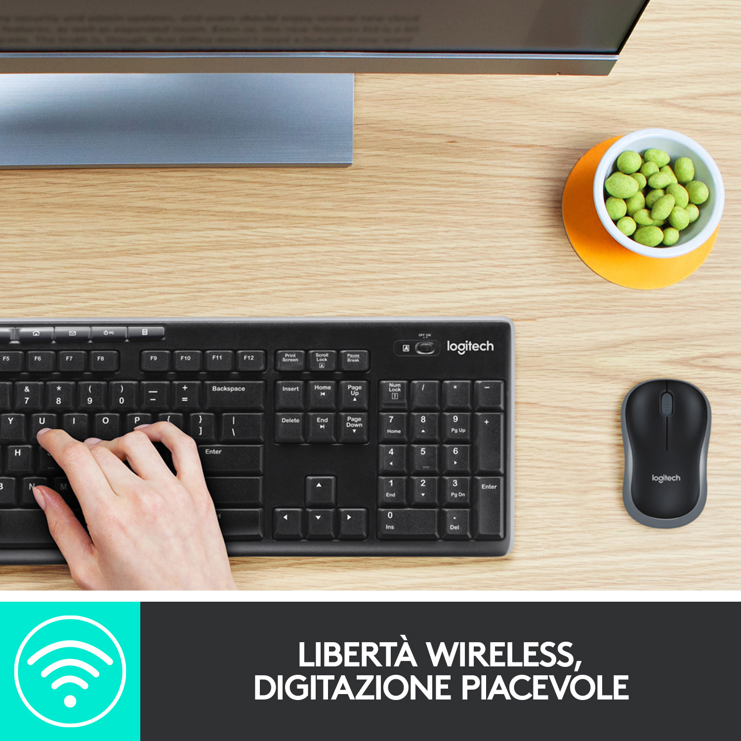 Tastiera e mouse Logitech neri su una scrivania di legno. Una ciotola di snack verdi e un'icona wifi.