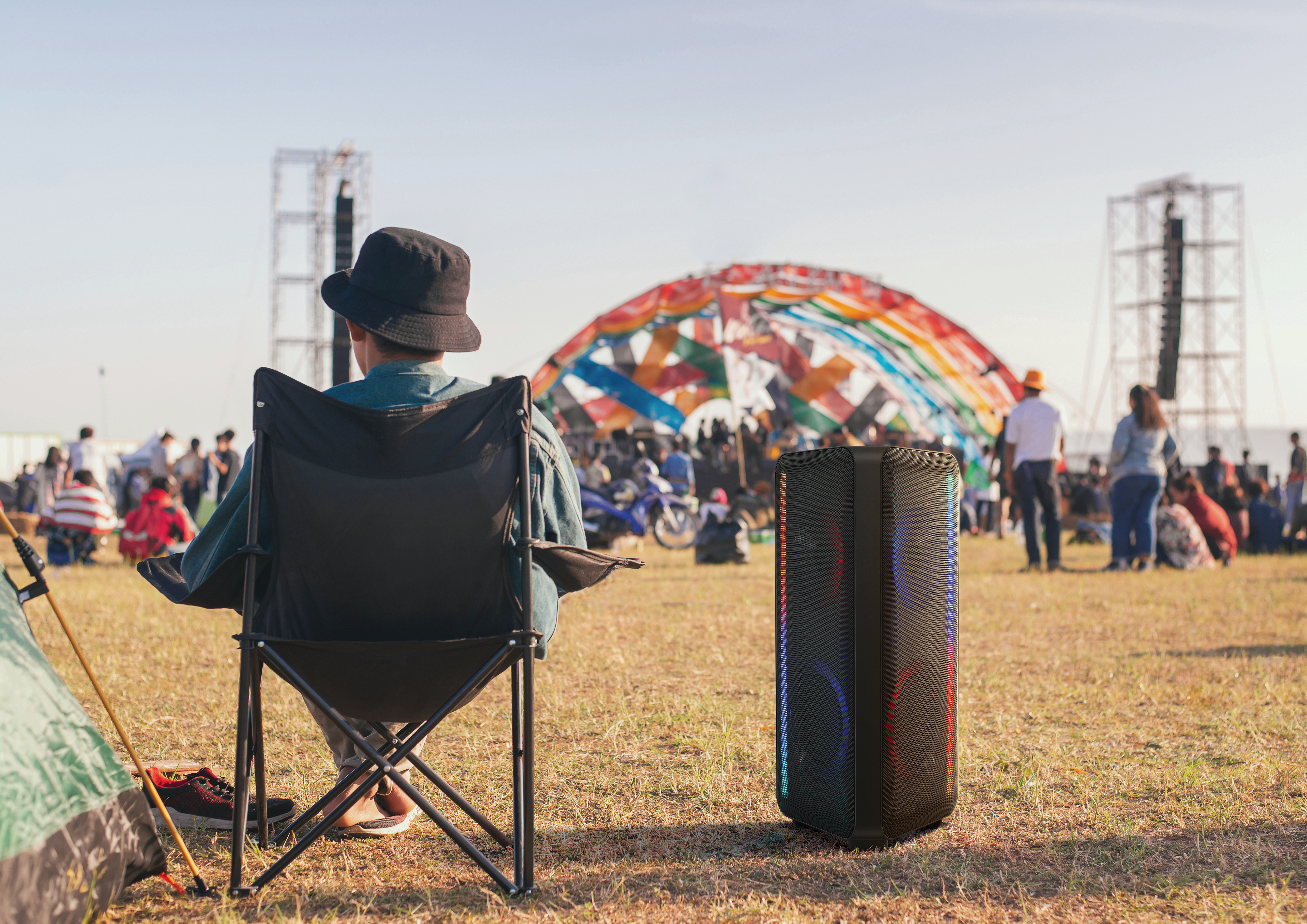 Eine Person sitzt in einem Klappstuhl in der Nähe eines Lautsprechers bei einer Outdoor-Veranstaltung.