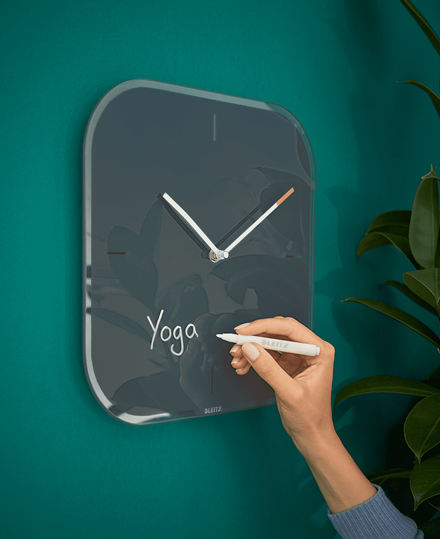 Óra türkiz falon, rajta a "Yoga" szóval. Egy kéz tart egy tollat.
