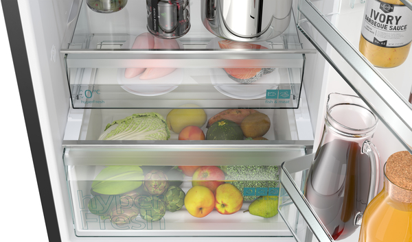 Offener Kühlschrank mit Obst, Gemüse und Fleisch in Schubladen und Flaschen an der Seite.