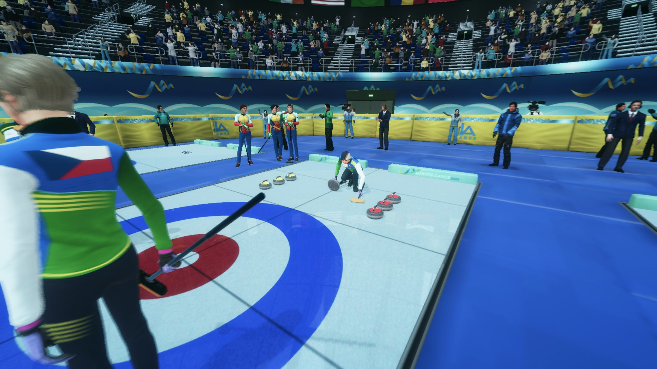 Partita di curling in corso, giocatori, pietre e una folla in un'arena blu.