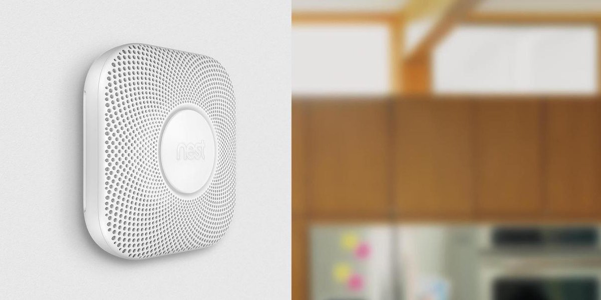 Un détecteur de fumée Nest blanc monté sur un mur, avec un arrière-plan en bois flou.