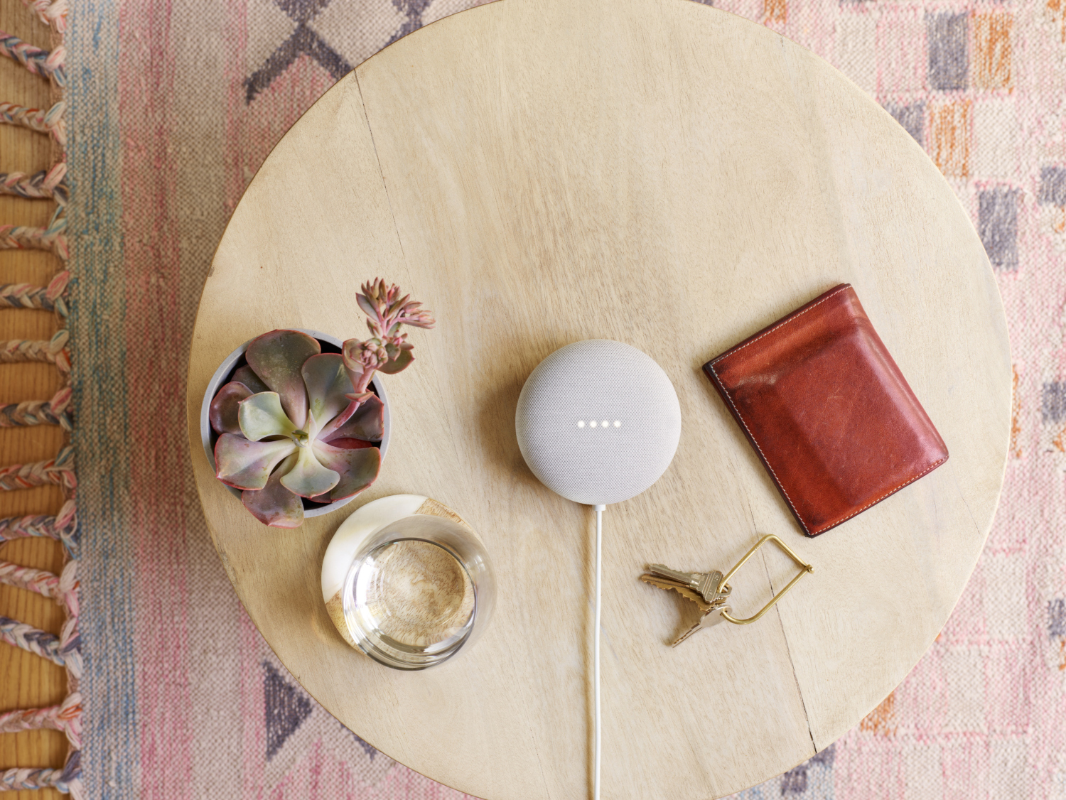 Un petit haut-parleur intelligent gris sur une table en bois avec des plantes, un portefeuille et des clés.