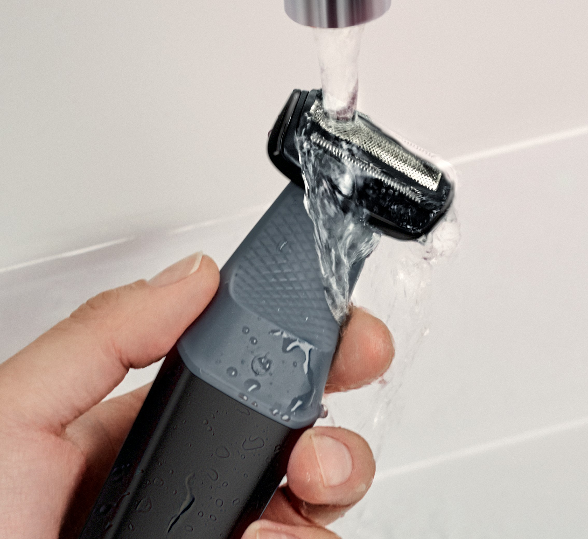 Una mano sosteniendo una afeitadora eléctrica bajo agua corriente.