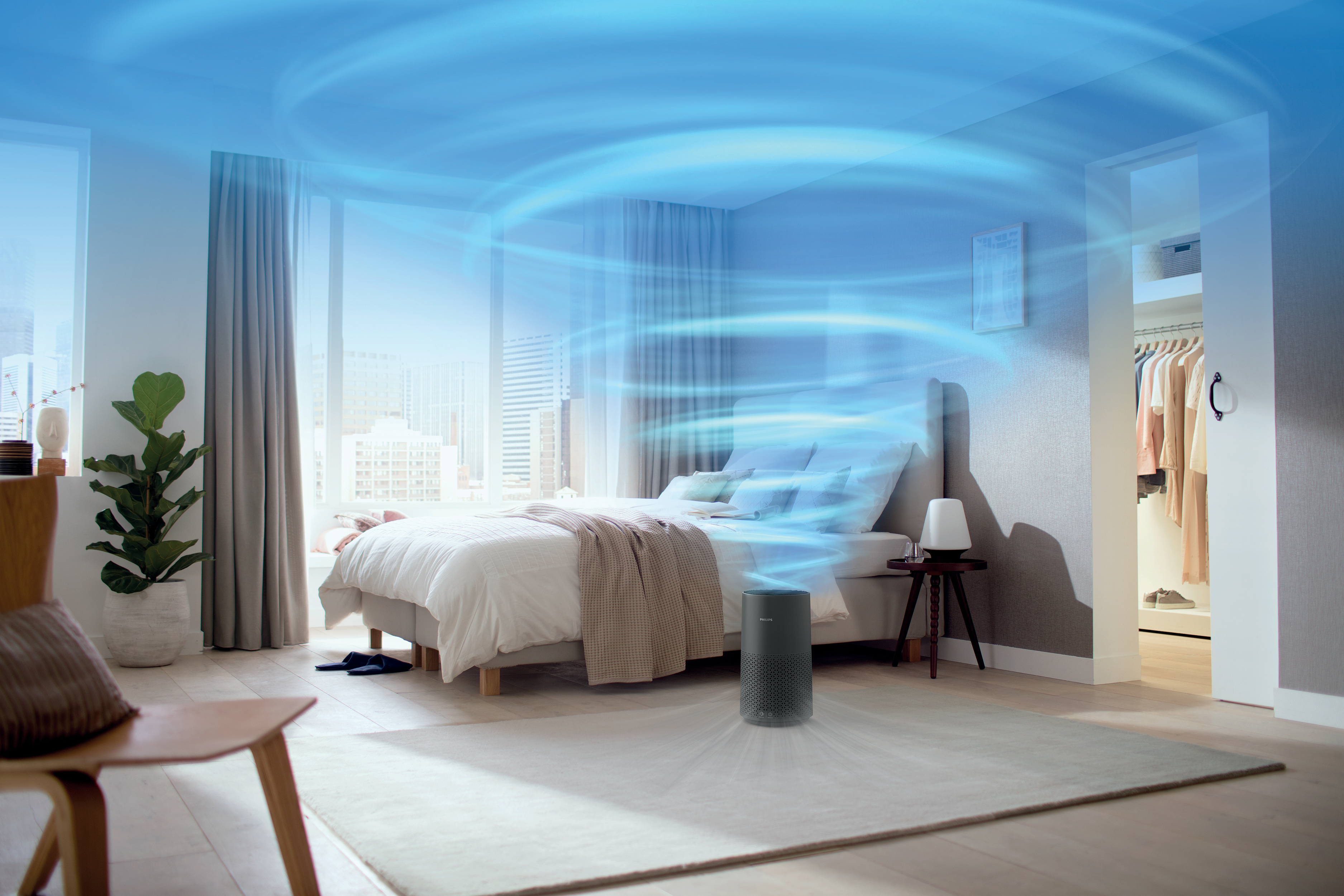Ein Luftreiniger in einem Schlafzimmer mit Bett, Stuhl und Fenster. Blaue Luft wirbelt darum herum.