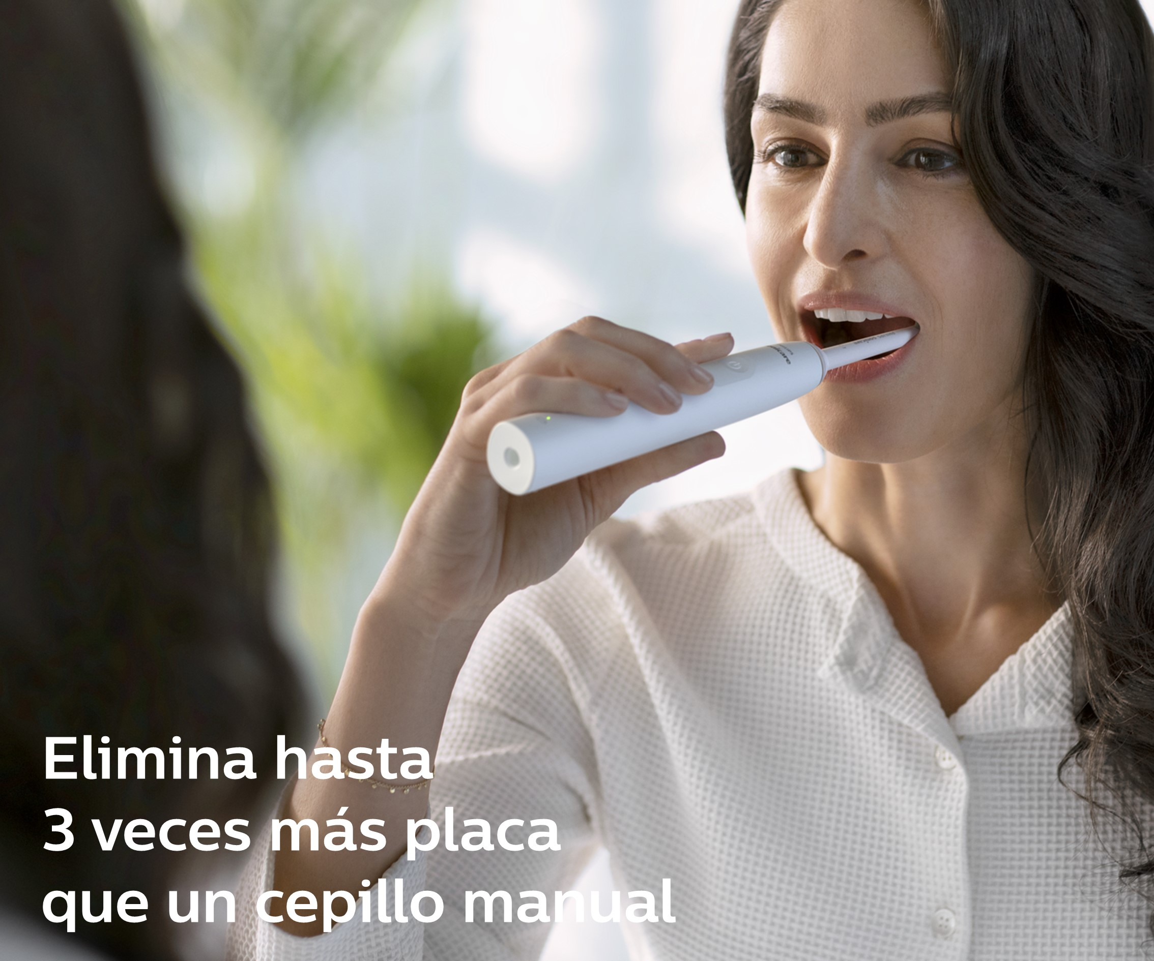 Mujer cepillándose los dientes con un cepillo de dientes eléctrico blanco frente a un espejo.