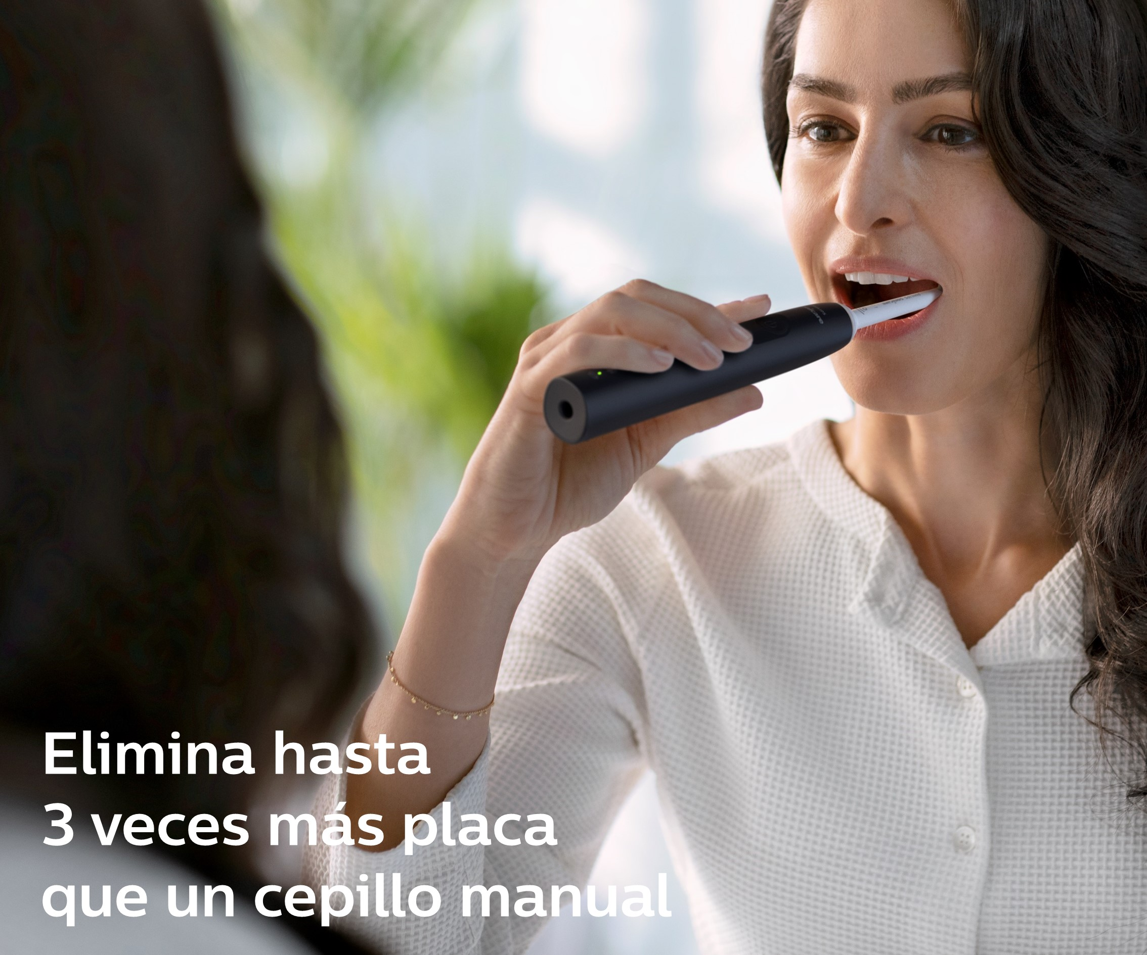 Mujer cepillándose los dientes con cepillo eléctrico negro frente al espejo.