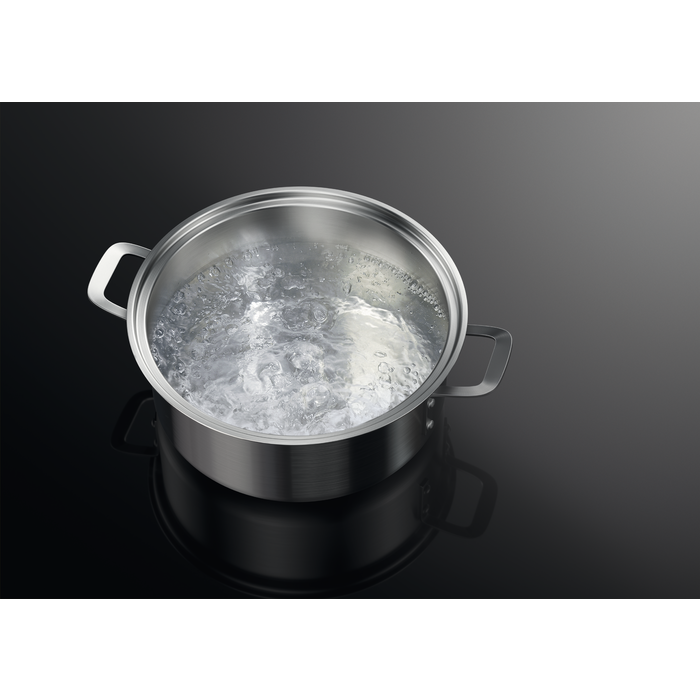 Una olla de acero inoxidable con agua hirviendo sobre una superficie negra.