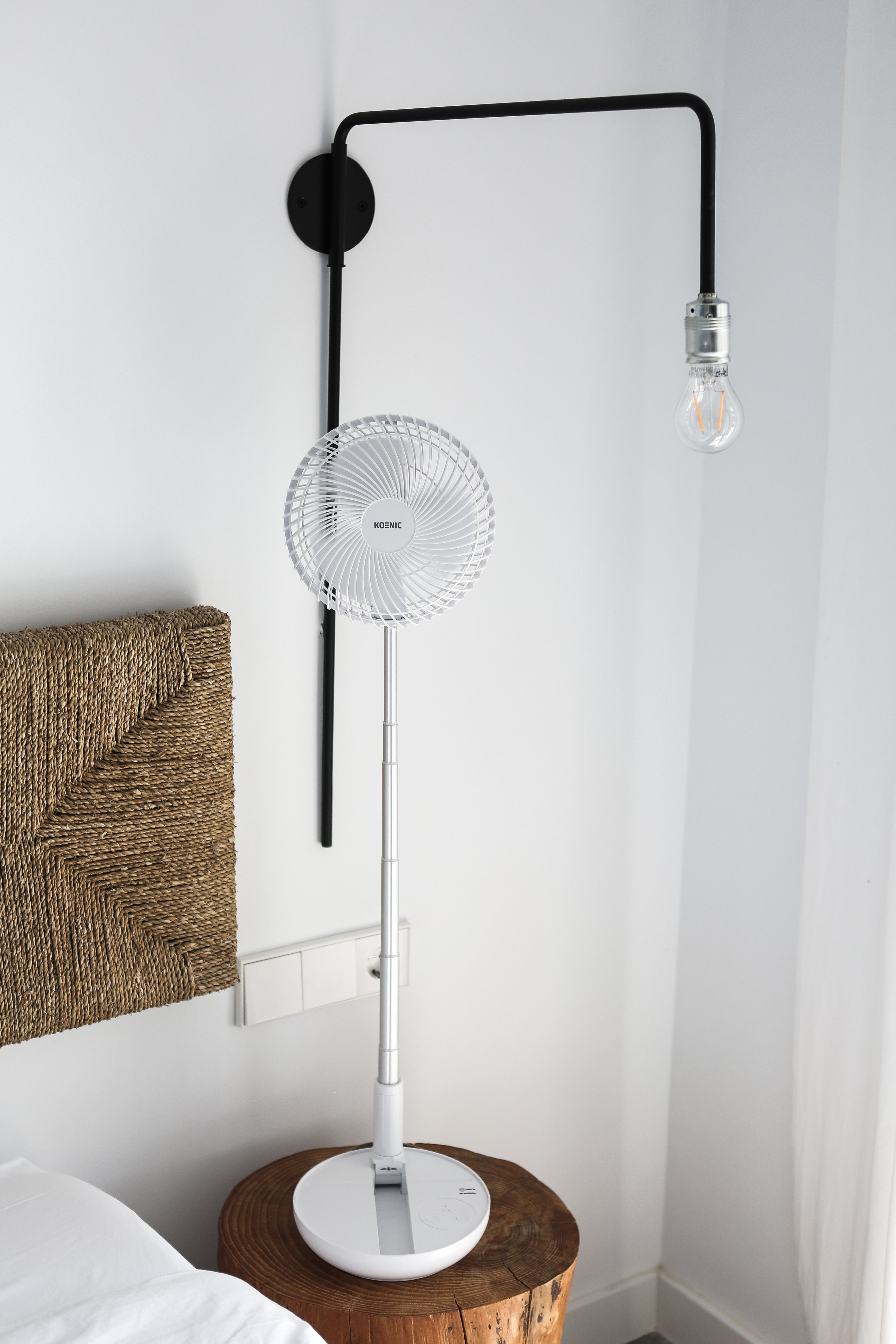 Álló fehér ventilátor lámpával és ággyal a háttérben.