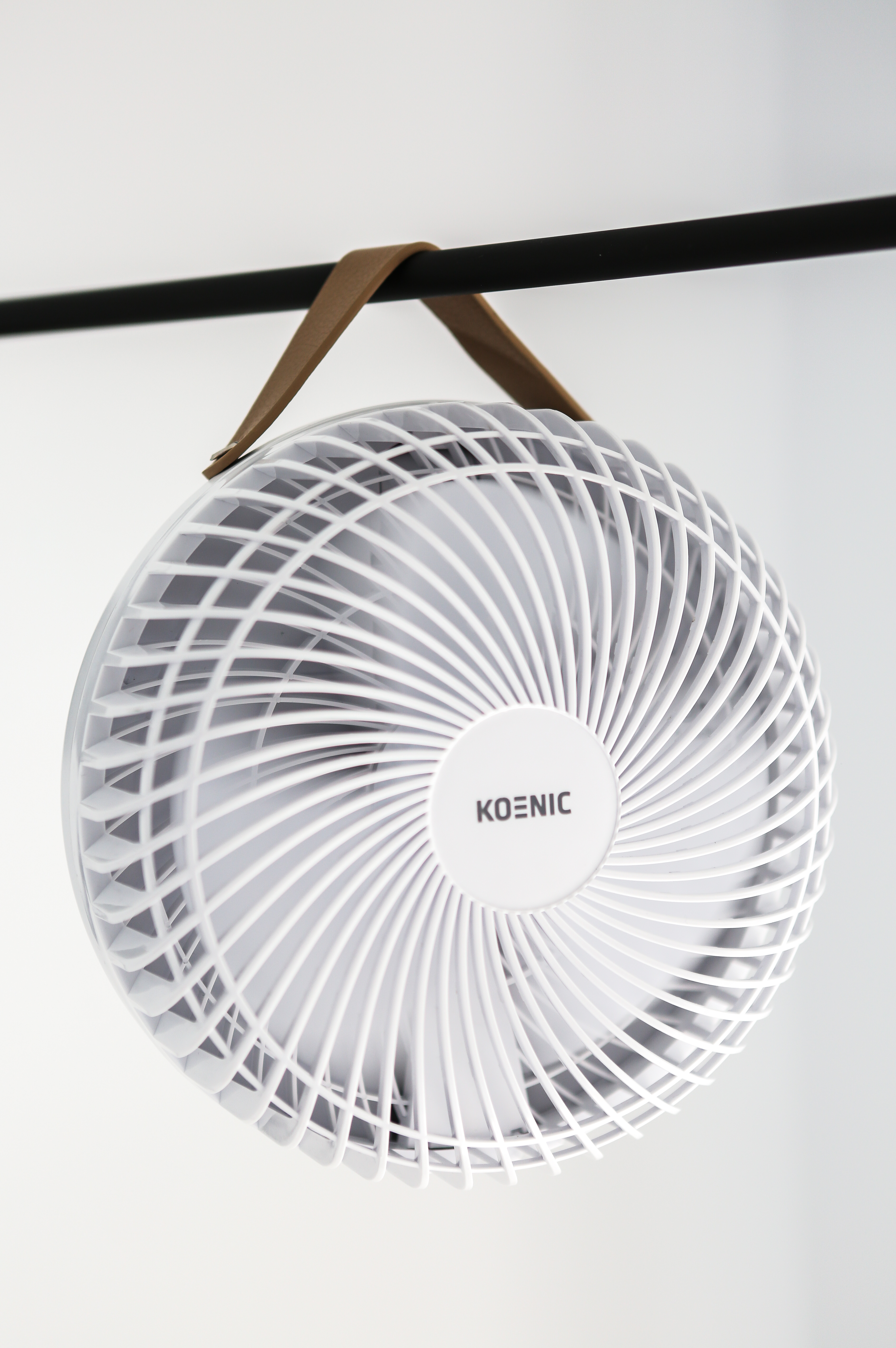Fehér kerek ventilátor barna fogantyúval, fekete rúdon lógva.