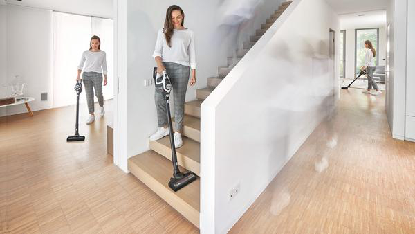 Eine Frau saugt eine Treppe und einen Flur mit einem kabellosen Staubsauger.