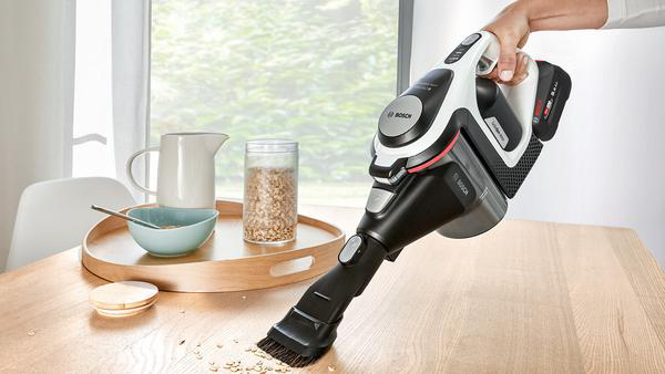 Handstaubsauger auf einem Holztisch, der Krümel aufsaugt.