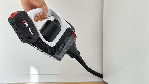 Eine Hand hält einen kabellosen Staubsauger. Er ist schwarz, weiß und hat eine rote Batterie.