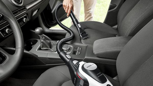 Person saugt einen Innenraum eines Autos. Staubsauger in Gebrauch, mit schwarzem Schlauch und weißem Gehäuse.