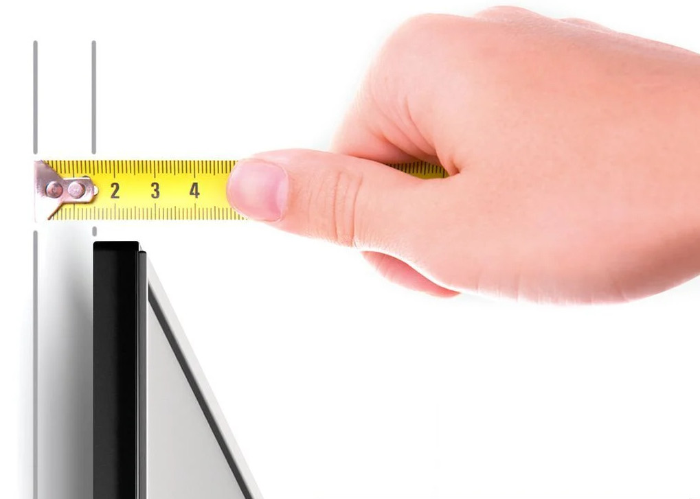 Une main mesure une surface noire avec un ruban à mesurer jaune sur fond blanc.