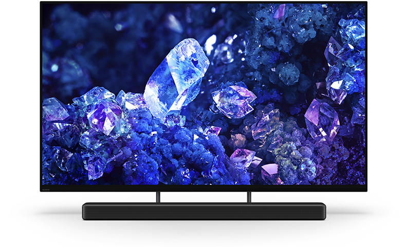 Egy fekete soundbar egy TV képernyő előtt, ami egy kék és lila kristályképet mutat.