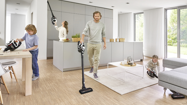 Eine Familie in einem modernen Zuhause, die Staubsauger benutzt. Menschen saugen Boden und Küche.