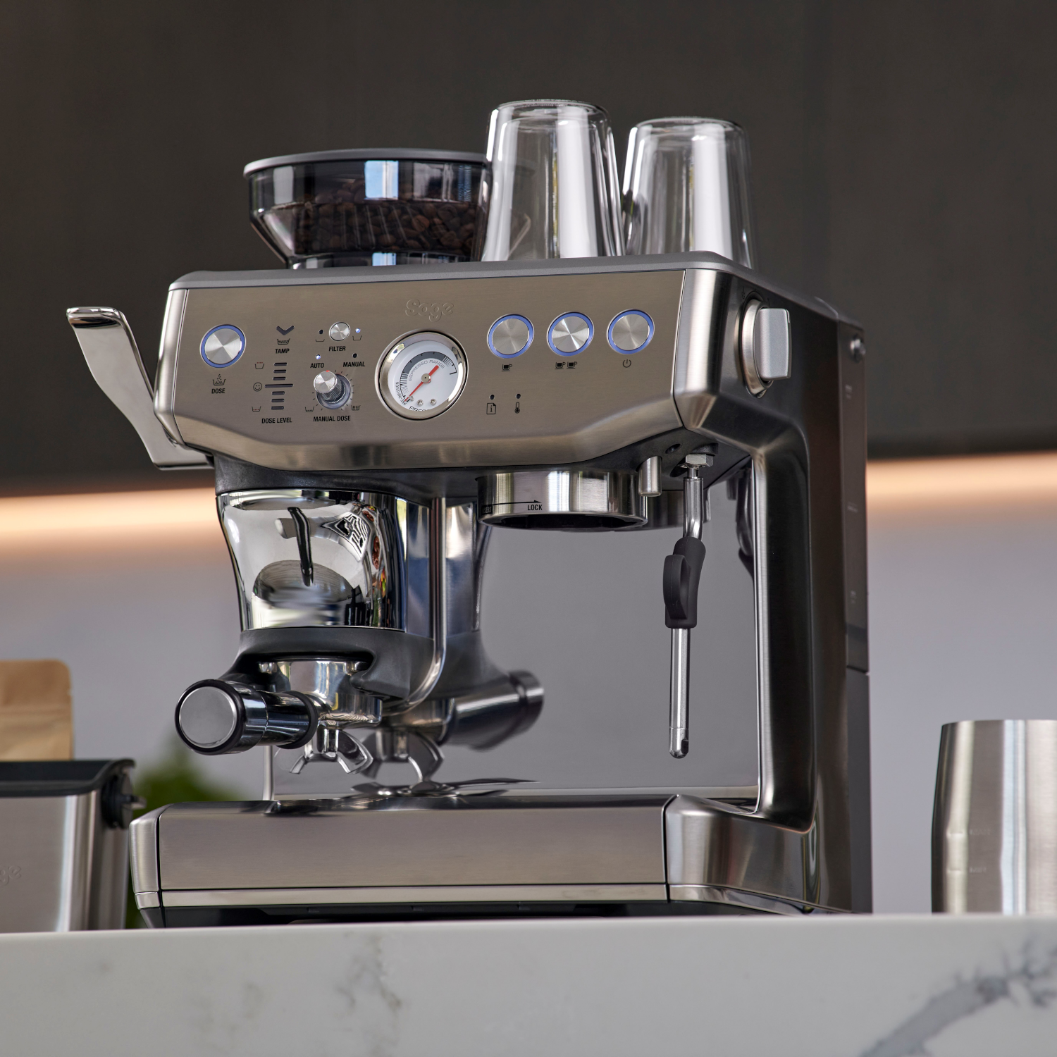 RVS espressomachine met accessoires. Twee glazen en een bonenmolen staan erop.