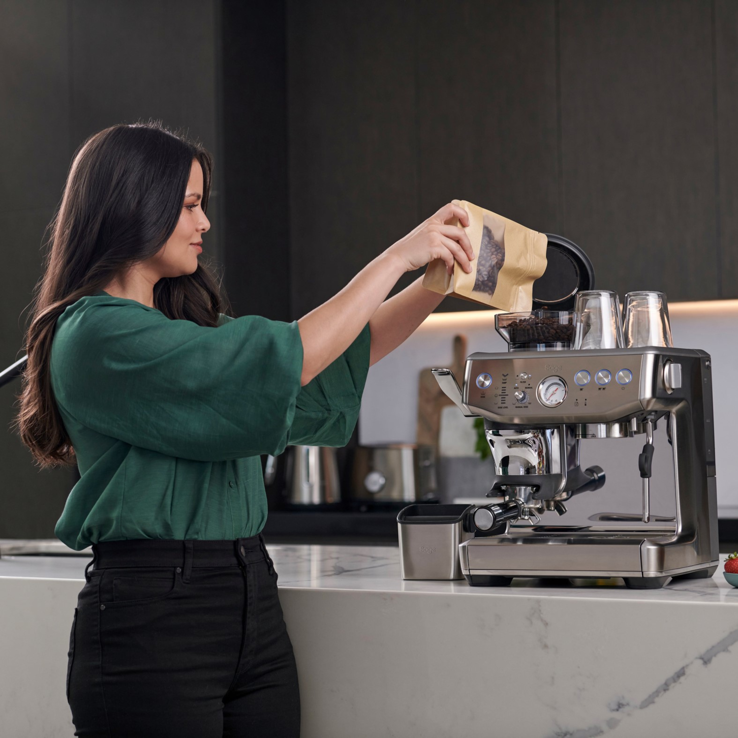 Een vrouw maakt koffie met een zilverkleurige espressomachine en giet er bonen in.