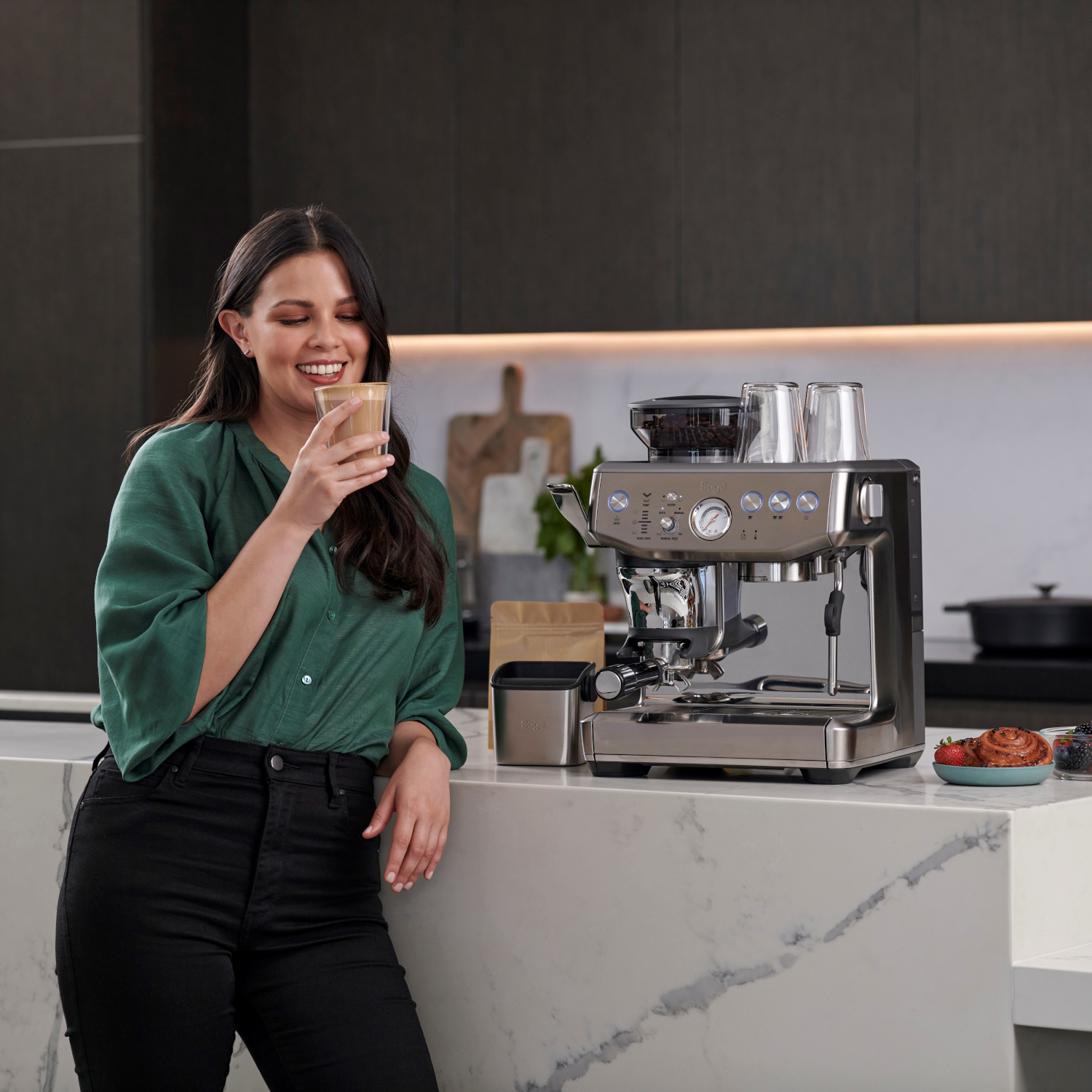 Een lachende vrouw die een koffiedrank vasthoudt in de buurt van een espressomachine.