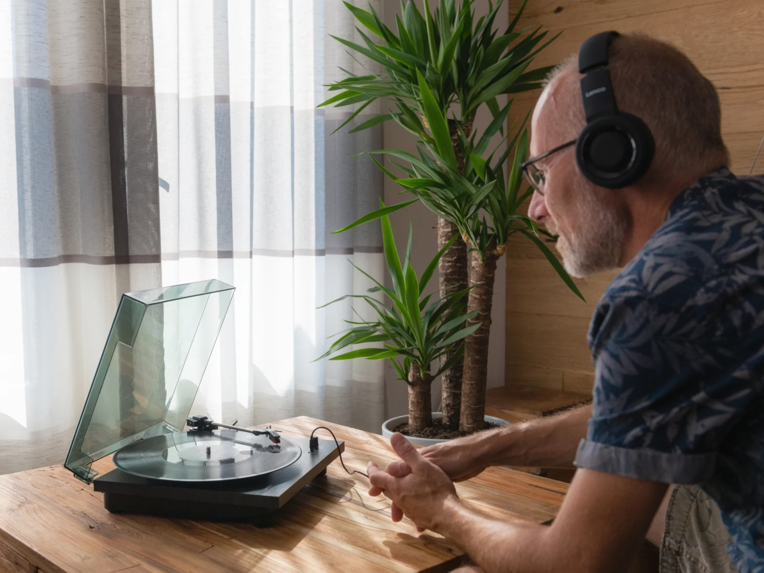 Un homme écoutant de la musique au casque, utilisant une platine. Une grande plante est visible derrière lui.