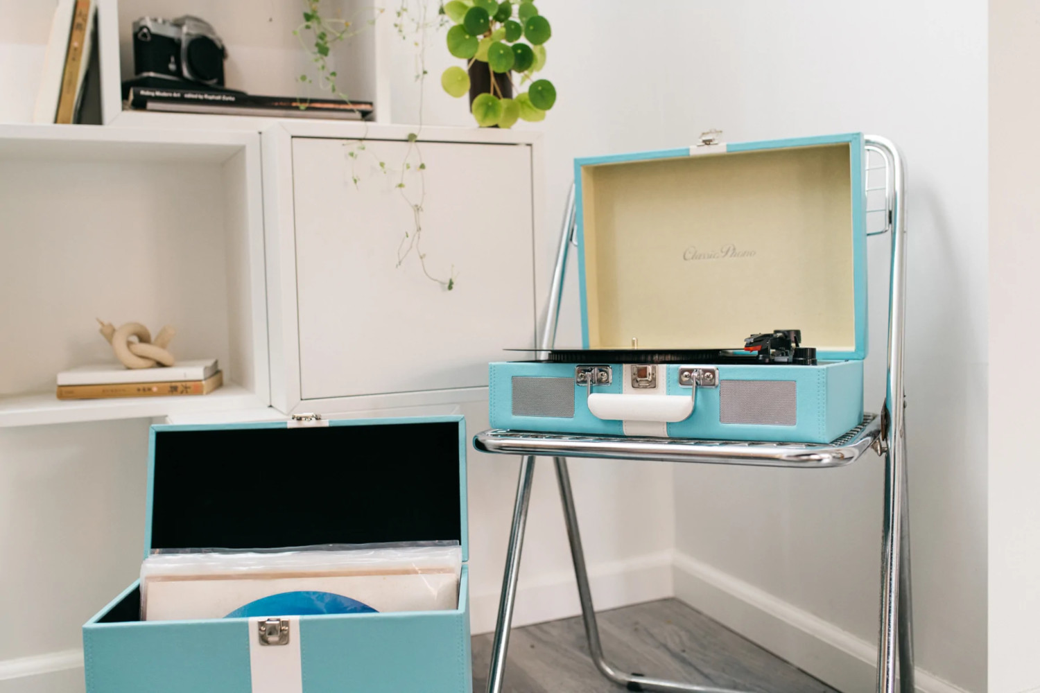 Platine sur une chaise argentée. Vinyles dans une boîte bleue. Étagère en arrière-plan.