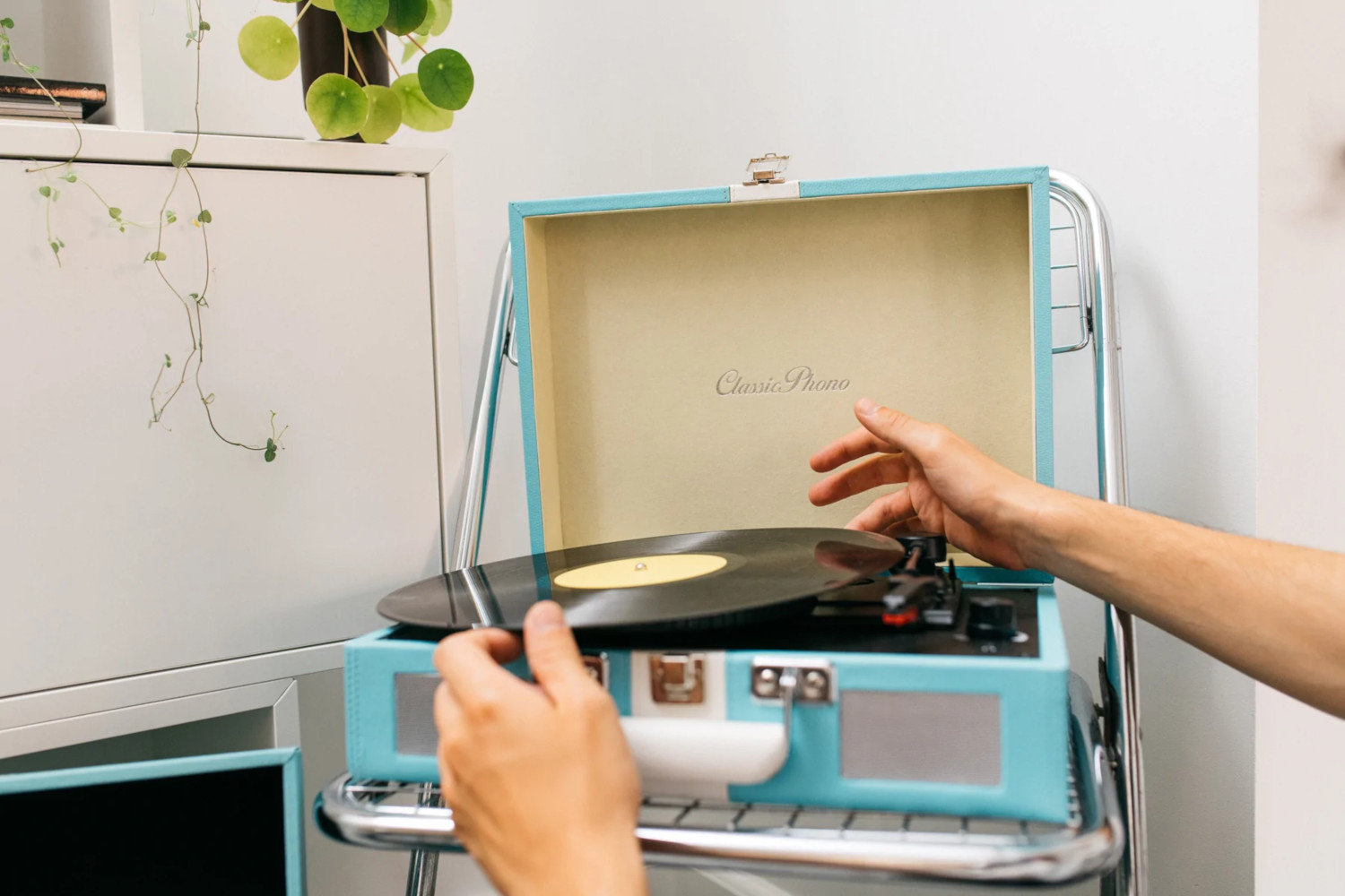 Mains plaçant un disque sur un tourne-disque bleu avec un couvercle ouvert.