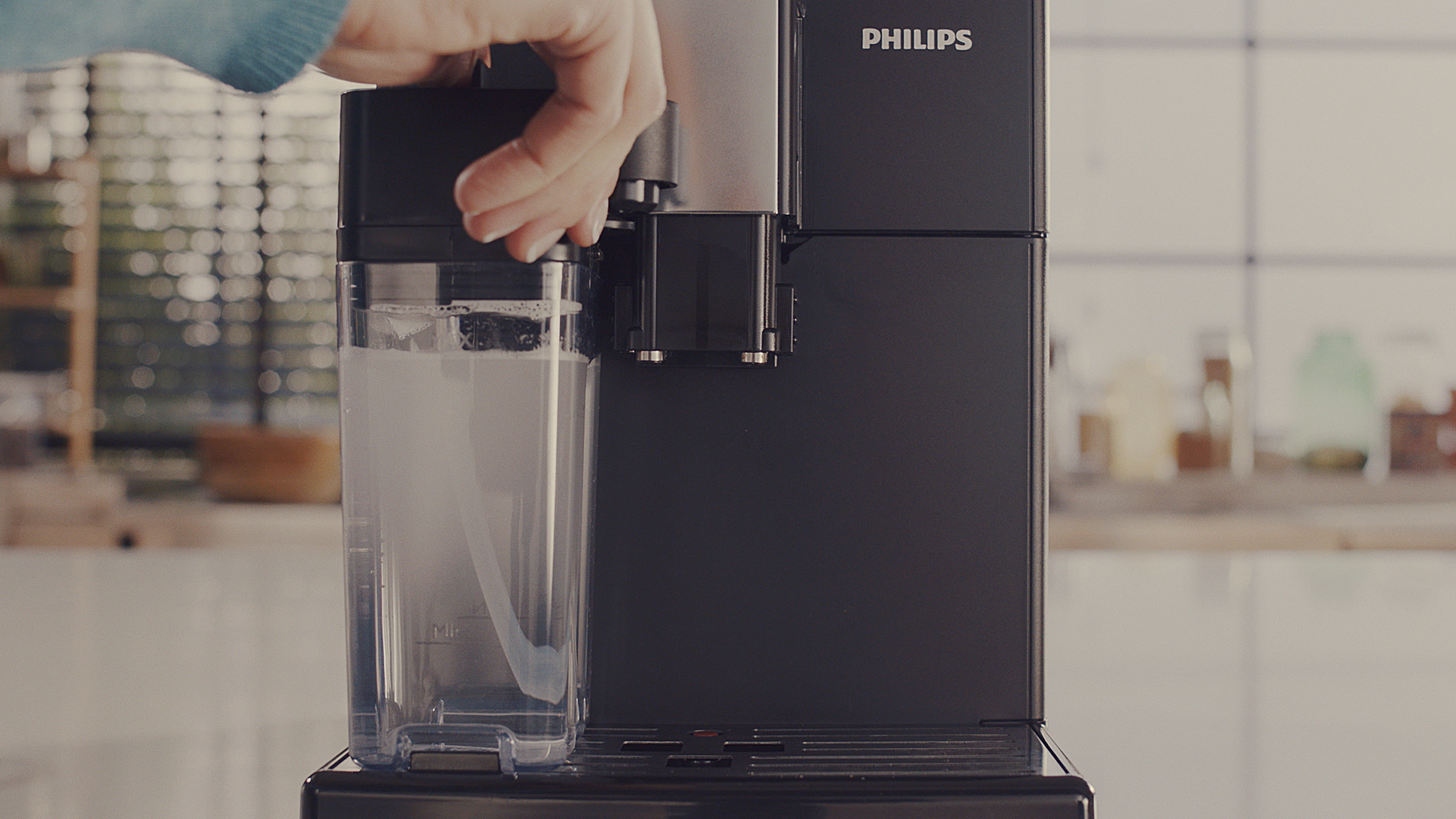 Persoon voegt water toe aan een zwarte Philips koffiemachine. Transparante watercontainer.