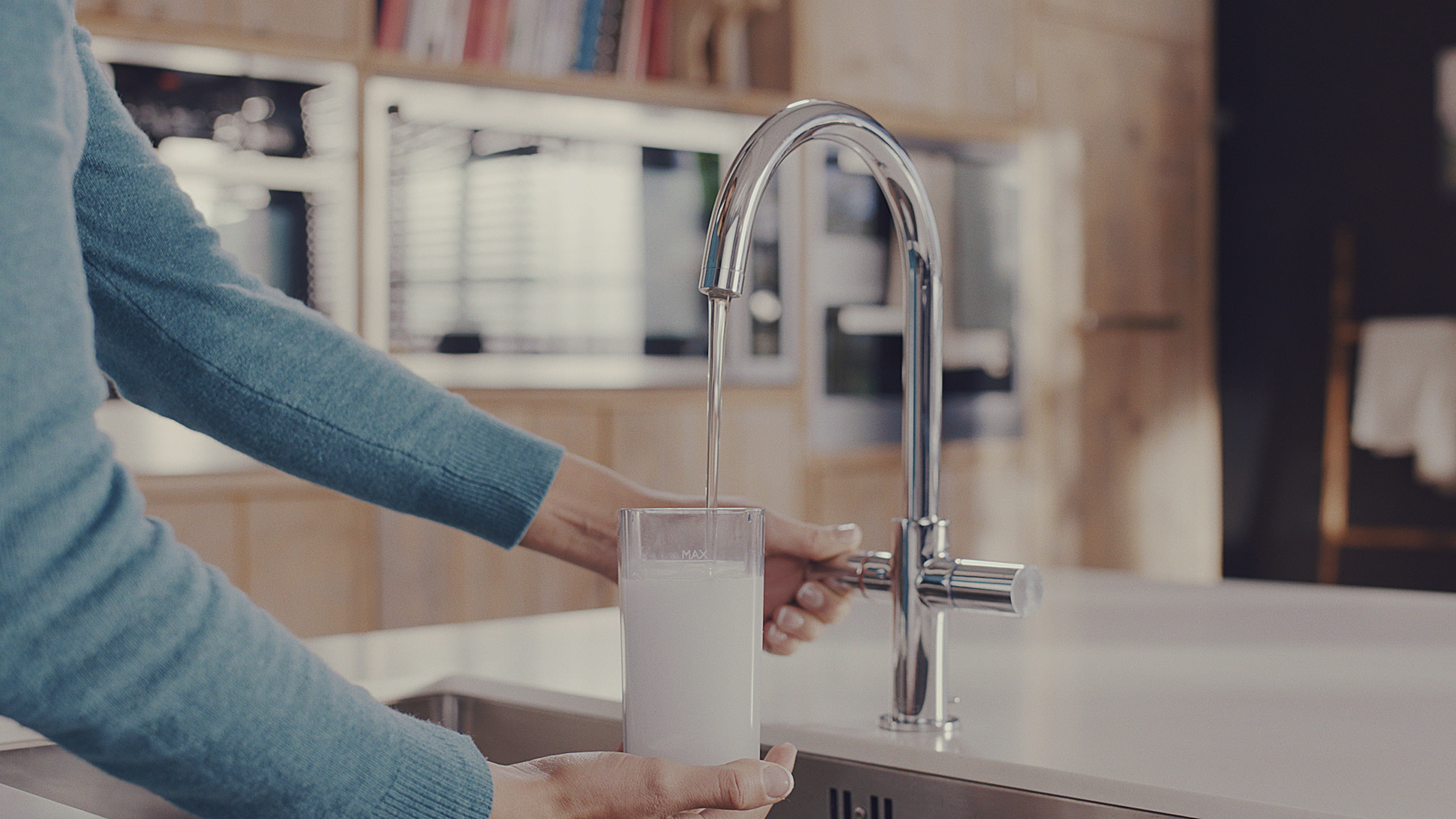 Een persoon vult een glas met water uit een chromen kraan in een moderne keuken.