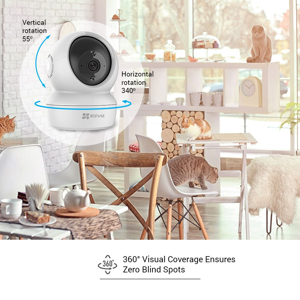Caméra de sécurité blanche avec couverture visuelle à 360°. Chats au premier plan, intérieur avec meubles.