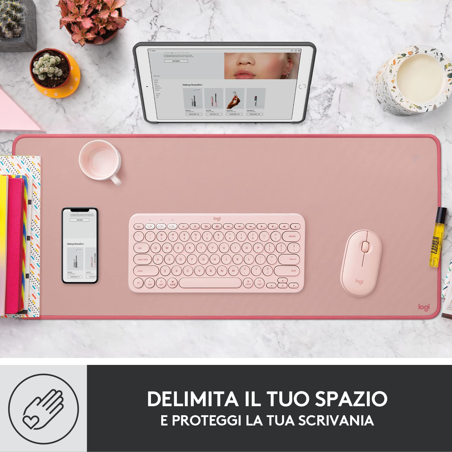 Configurazione scrivania rosa con tastiera, mouse, tablet, telefono e vari elementi.