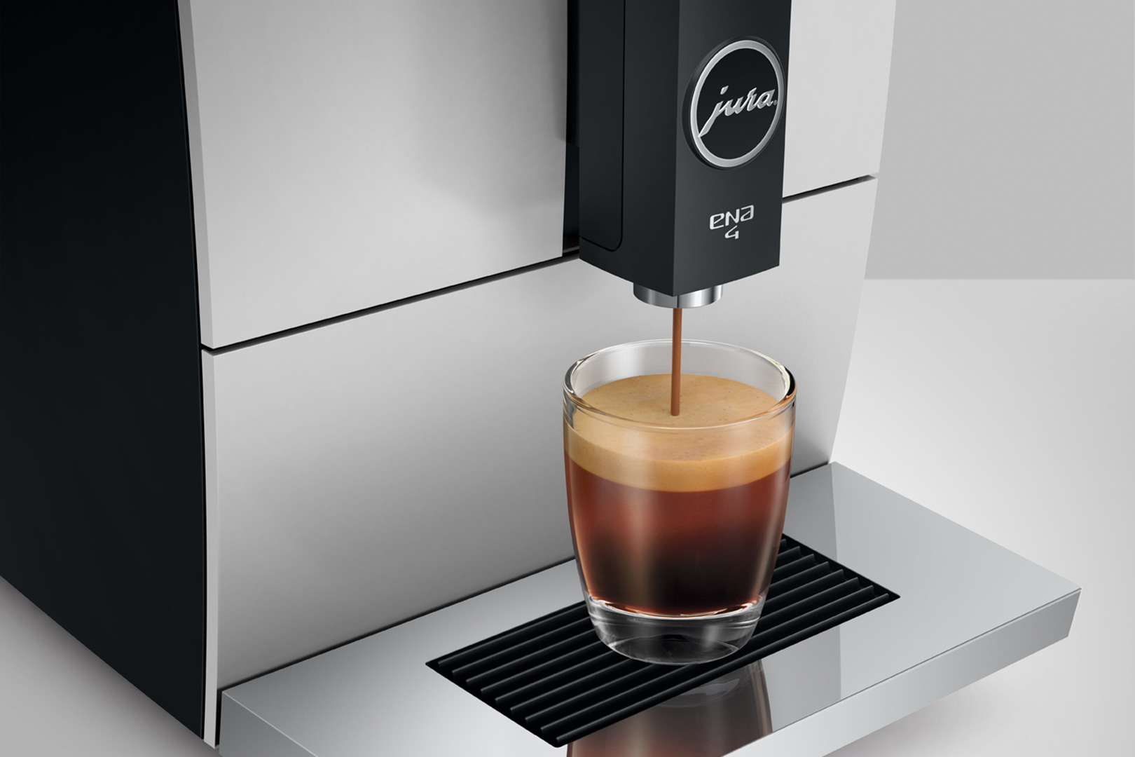Une machine à café Jura ENA 4 distribuant du café dans une tasse en verre, café brun foncé.
