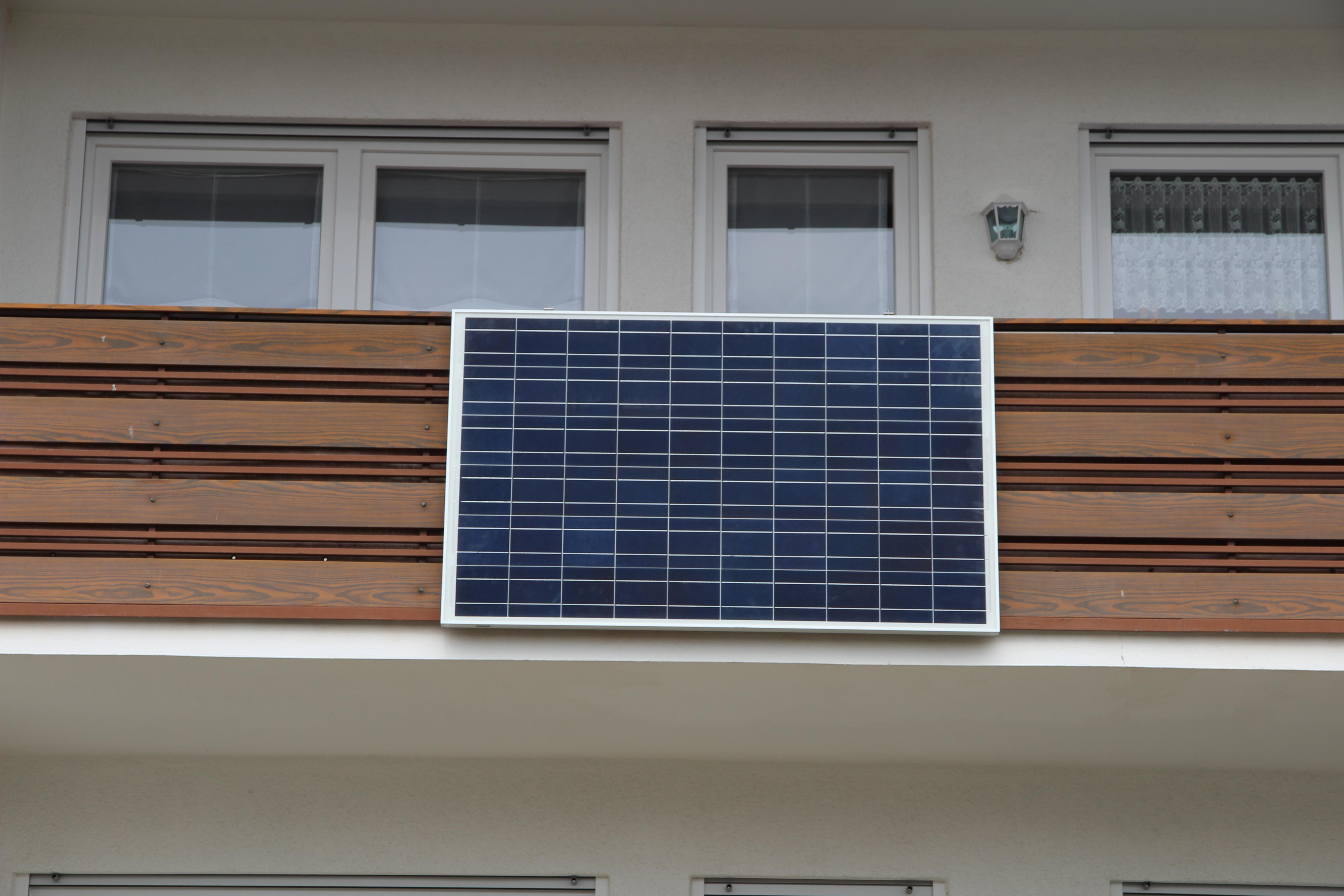 Solarpanel auf einem Balkon. Das Panel ist dunkelblau. Gebäude im Hintergrund.
