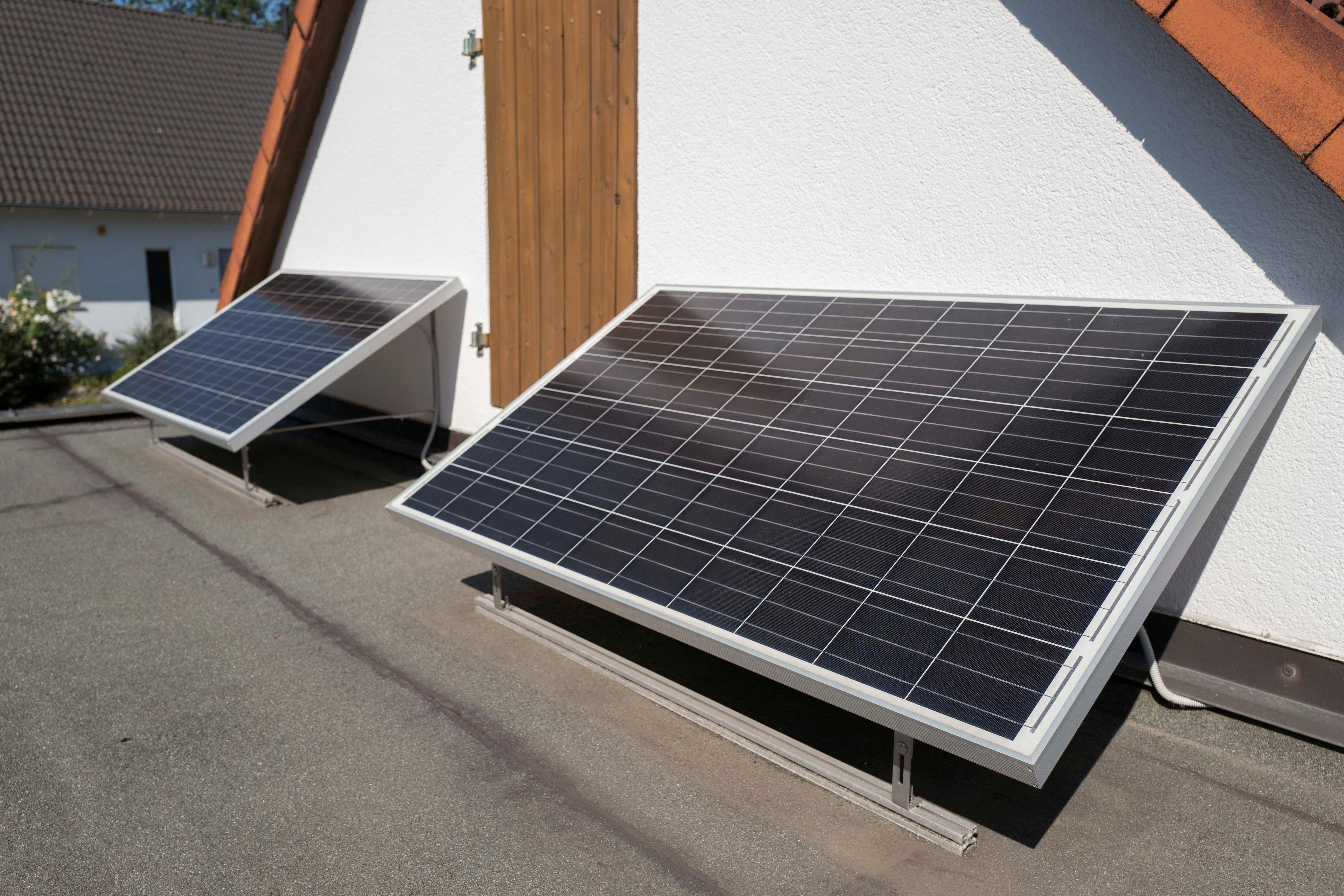 Zwei Solarmodule auf einem Dach montiert. Die Sonne reflektiert sich auf den Paneelen. Hintergrund: Haus und Himmel.