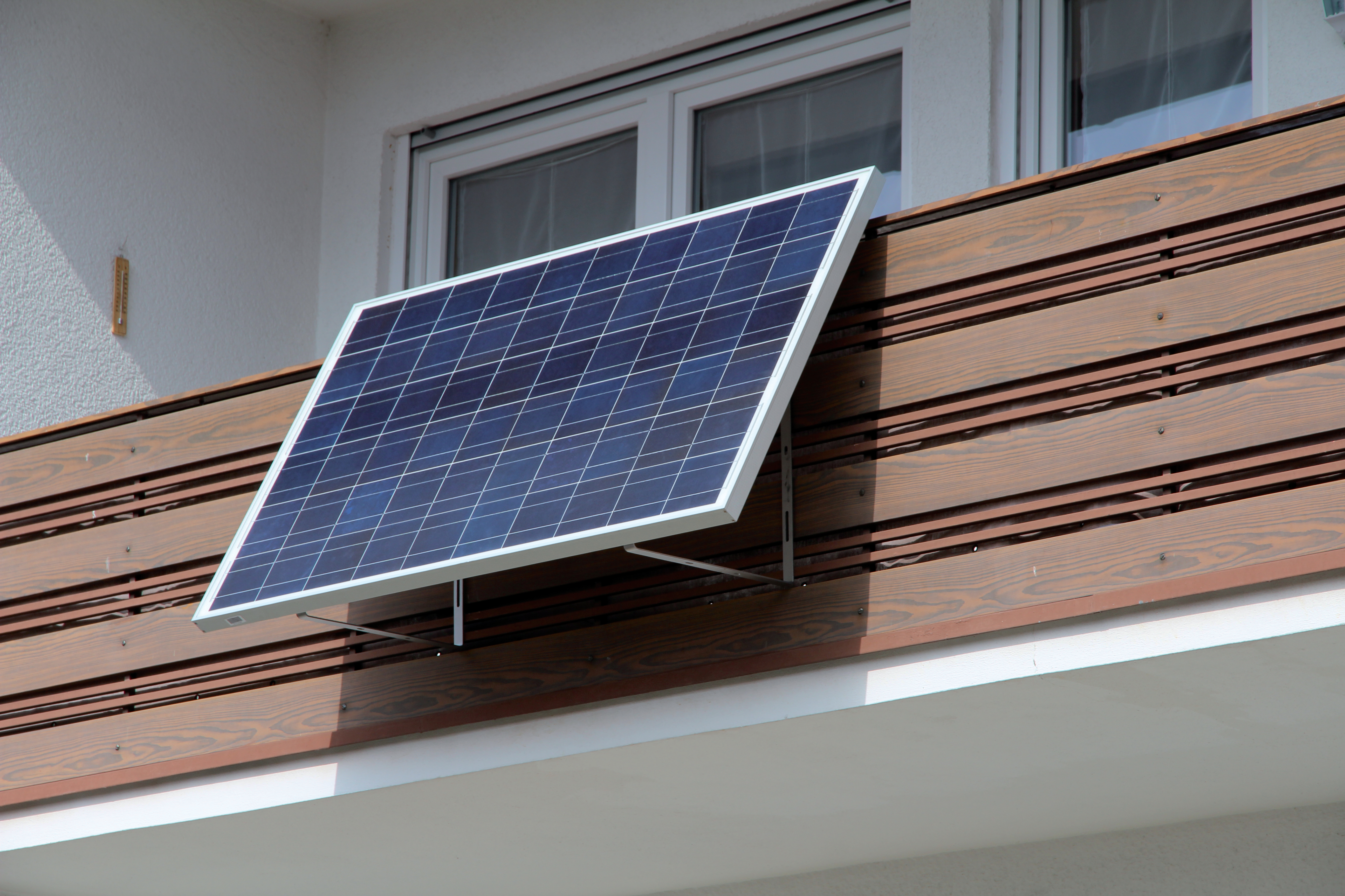 Ein Solarpanel, das an einem hölzernen Balkongeländer befestigt ist. Das Panel ist zum Himmel geneigt.