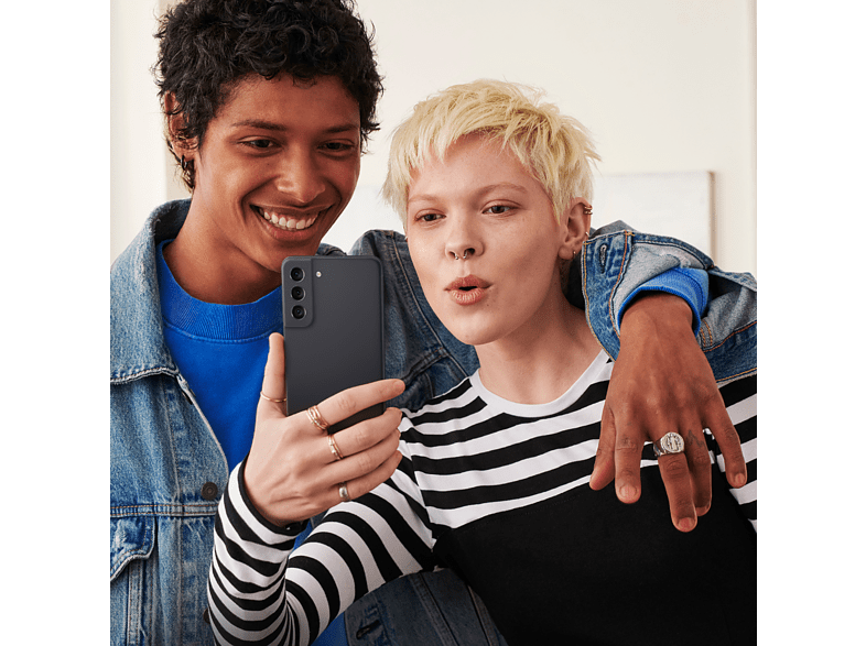 Dos personas se hacen un selfie con un teléfono negro; una sonríe, la otra hace una mueca.