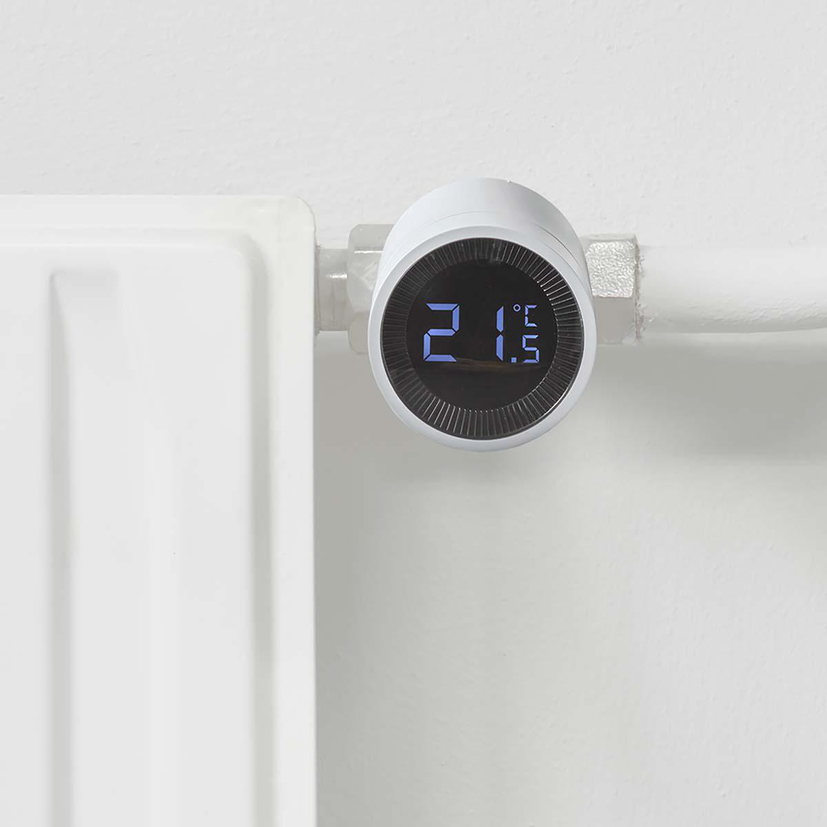 Weißes Smart-Thermostat an einer weißen Wand mit Heizkörper montiert.