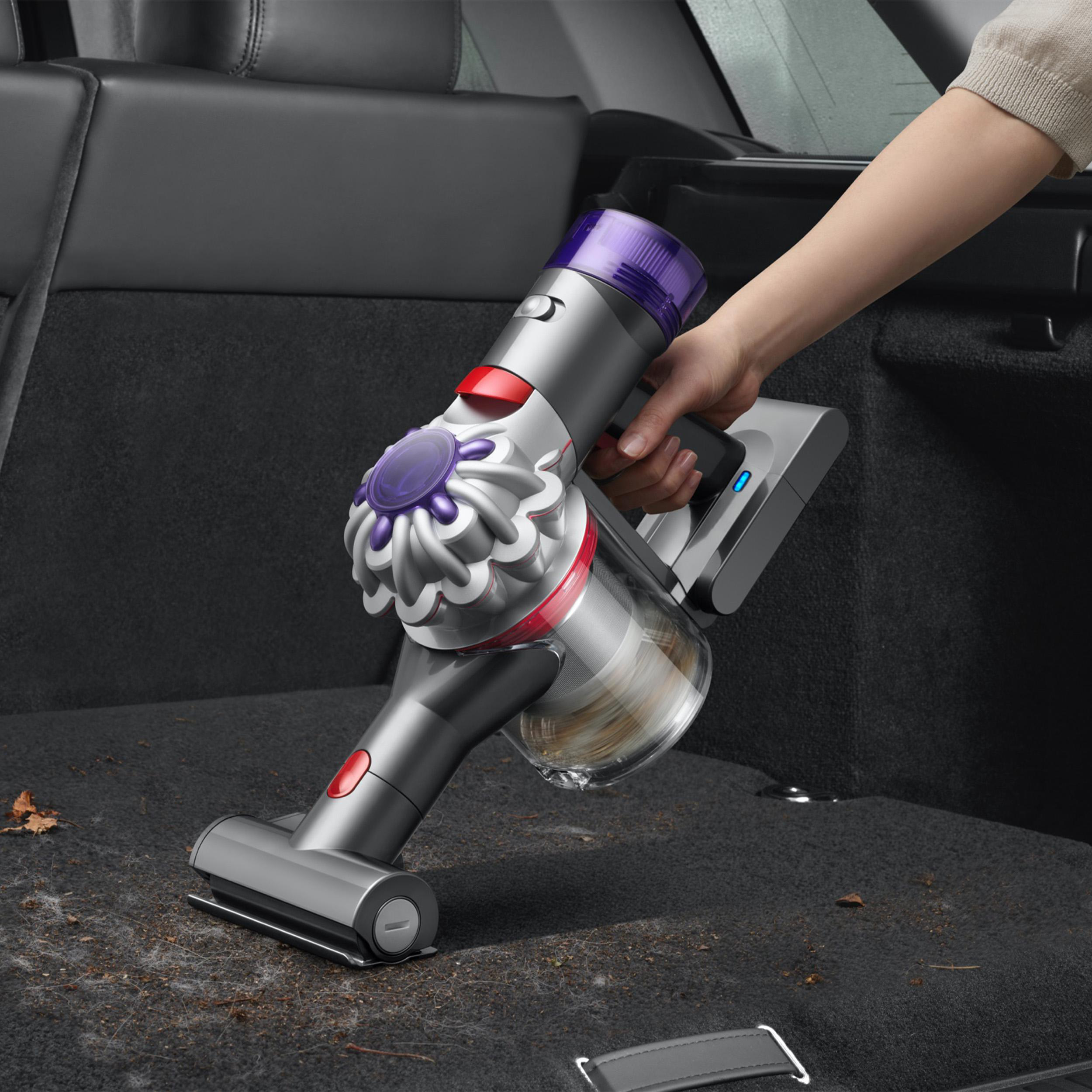 Hand staubsaugt einen Autositz. Dyson-Staubsauger in Gebrauch. Grau und lila.