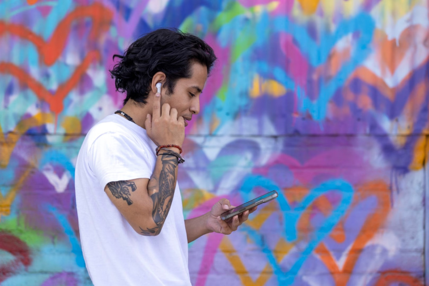 Un homme portant une chemise blanche tient un téléphone et un écouteur. Mur couvert de graffitis en arrière-plan.