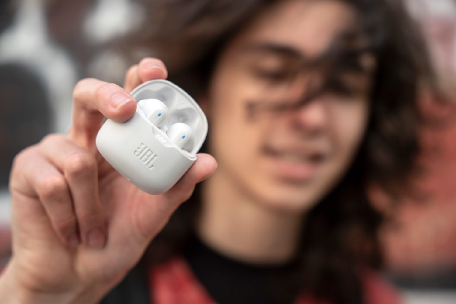 Een persoon die een witte case vasthoudt met twee witte oordopjes, het JBL-logo is zichtbaar.