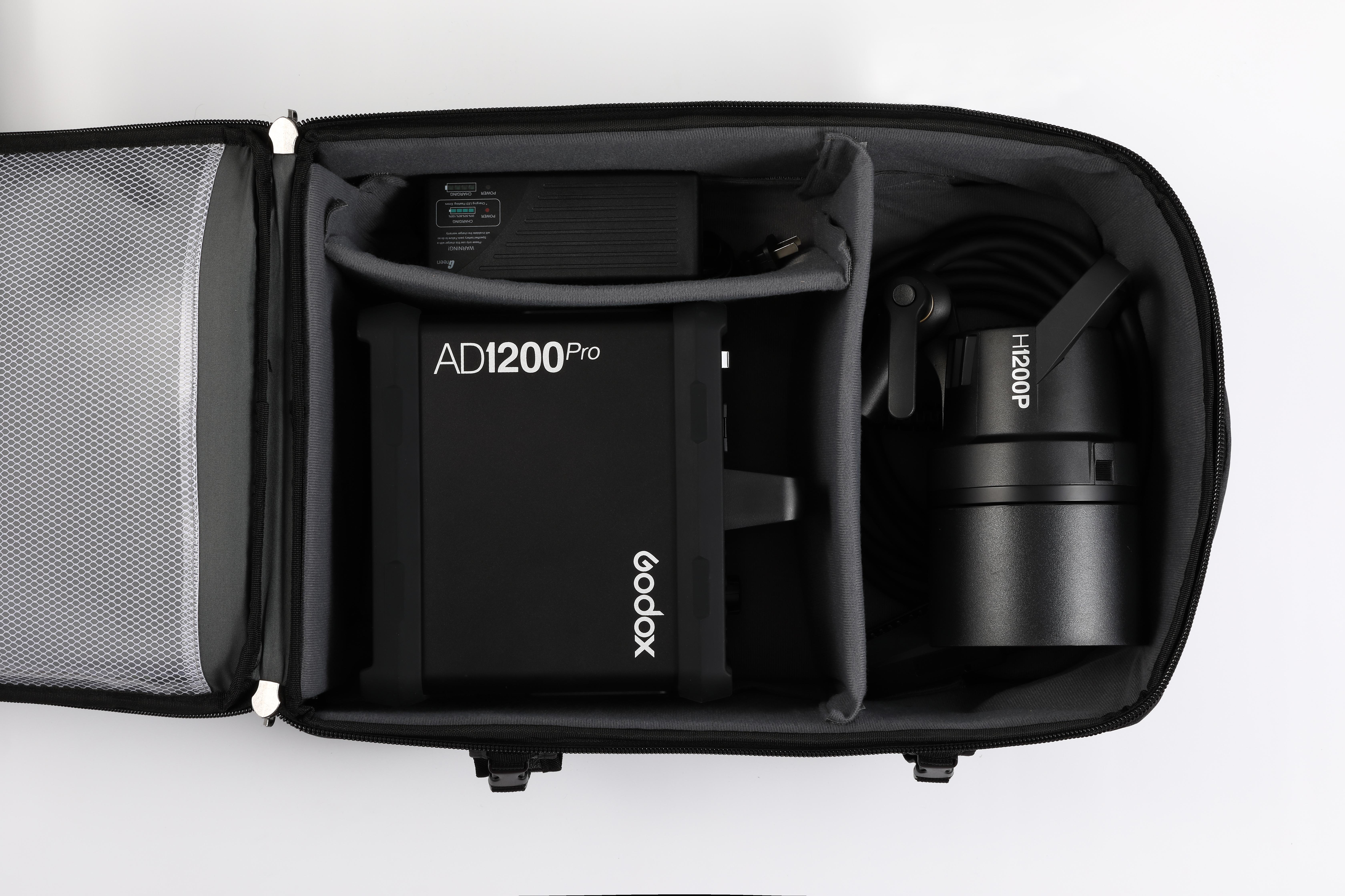 Schwarzes Godox AD1200 Pro Blitzlicht-Kit in einer grau-schwarzen Tasche mit Trennwänden und Zubehör.