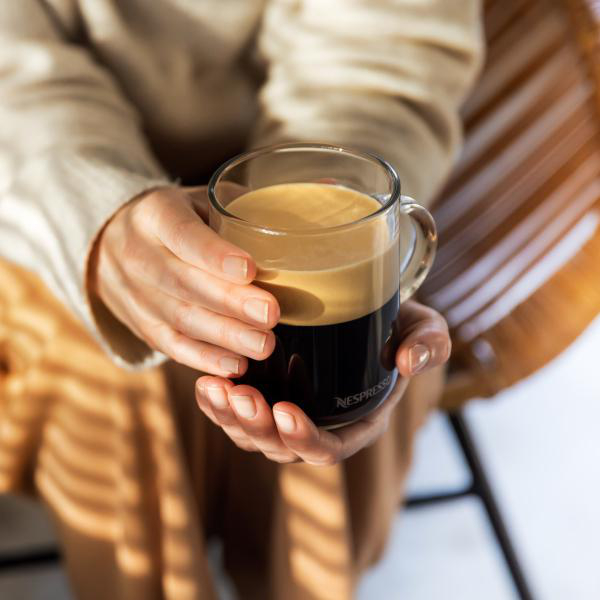 Eine Person hält eine Kaffeetasse mit Kaffee. Die Tasse ist klar, der Kaffee sichtbar.