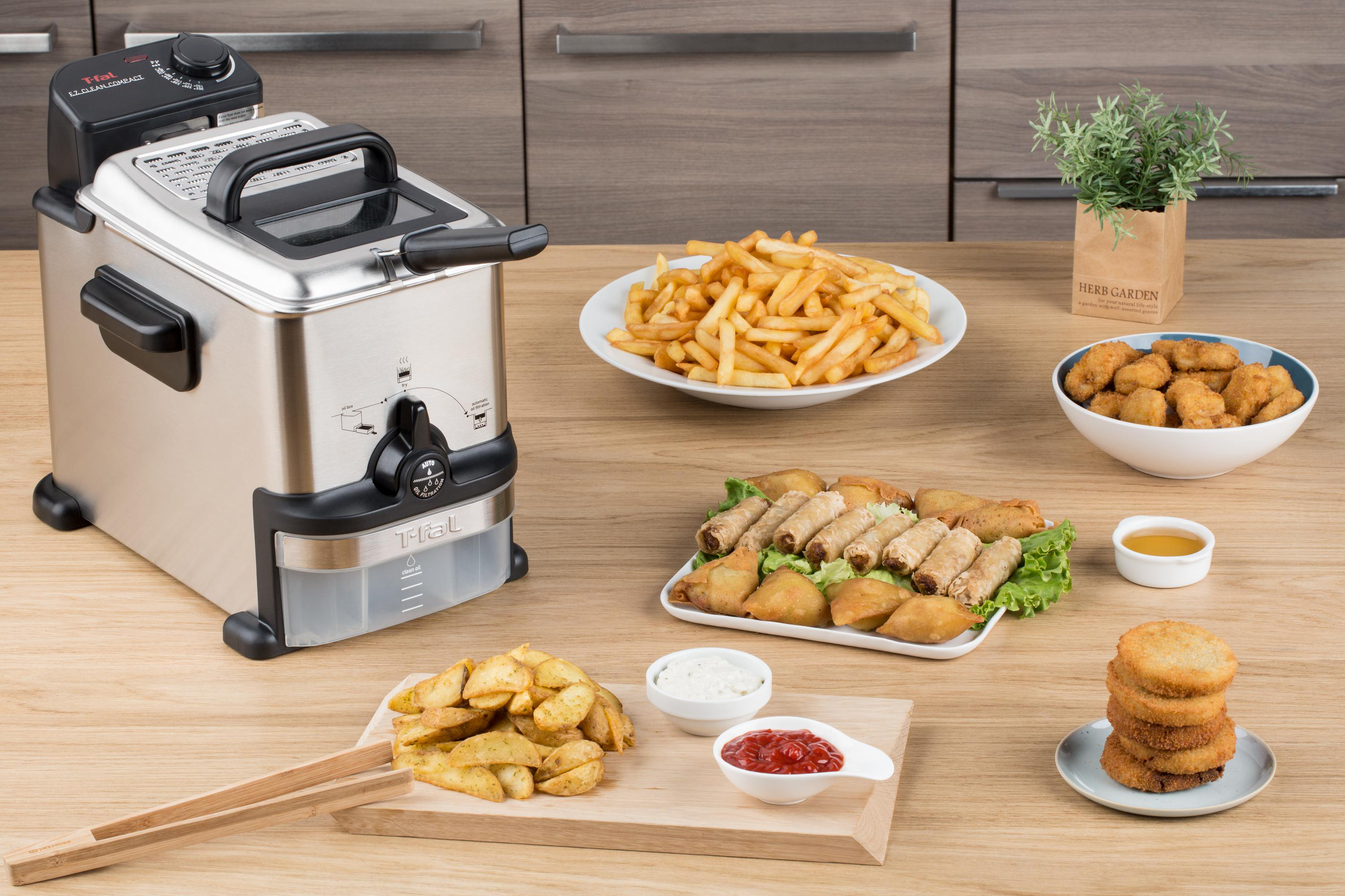 Eine Fritteuse mit gekochtem Essen: Pommes, Nuggets, Brötchen und Wedges, auf einem Holztisch.