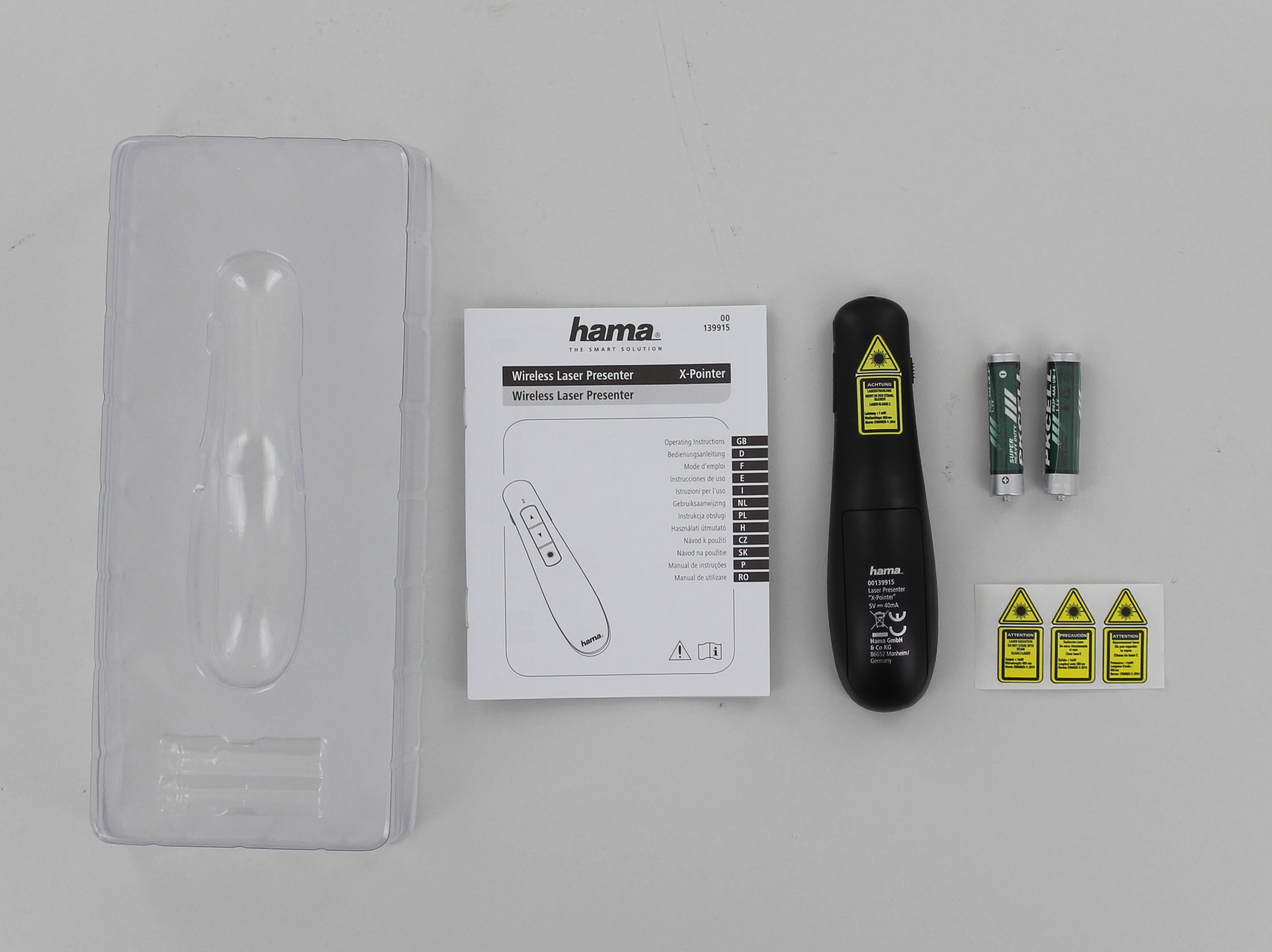 Presentador láser inalámbrico, pilas y manual de instrucciones sobre una superficie blanca.