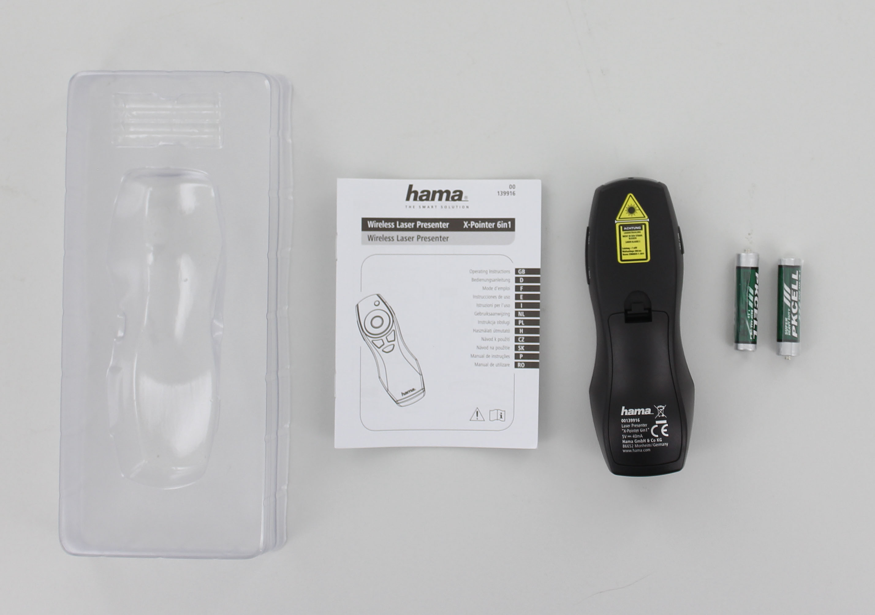 Kit de presentador láser inalámbrico Hama. Incluye presentador, pilas y manual, sobre superficie blanca.