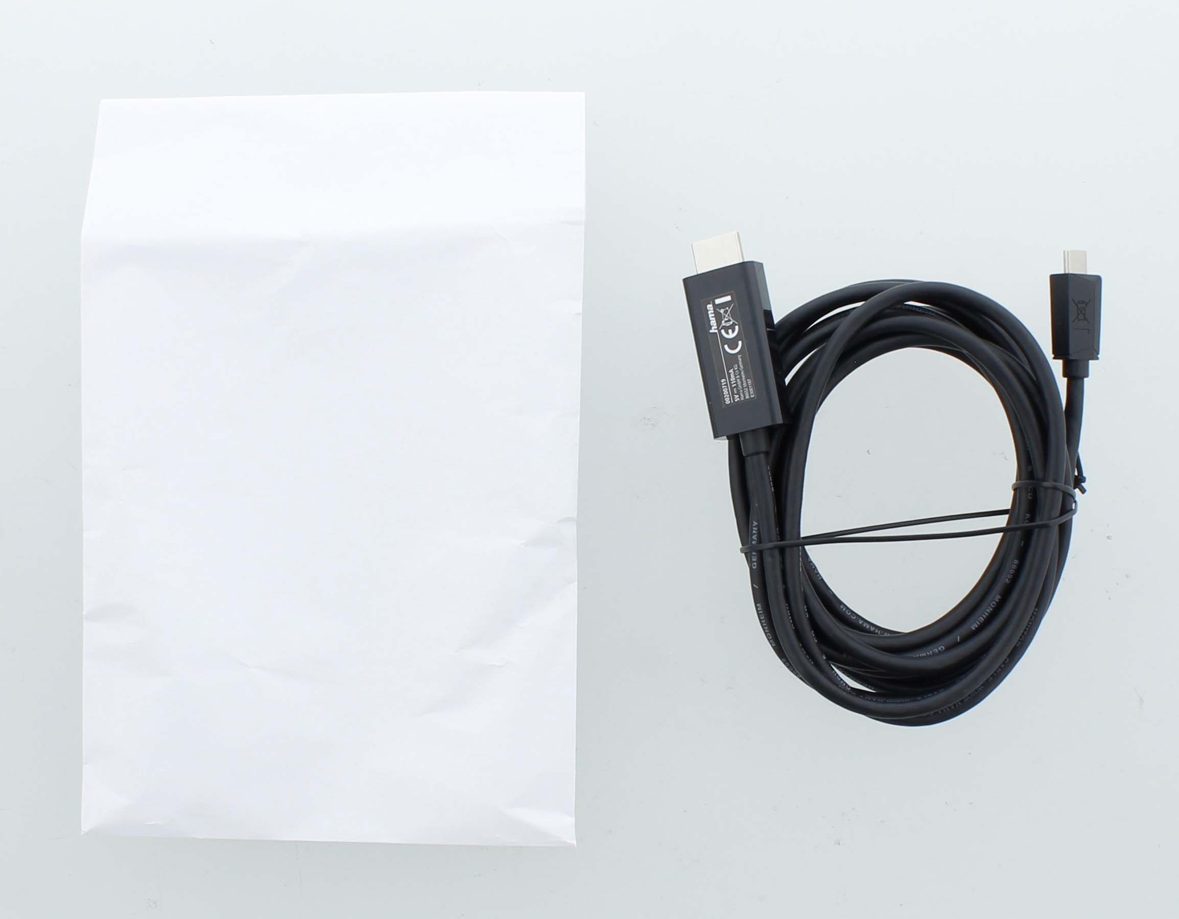 Una bolsa blanca y un cable negro con conectores se muestran sobre una superficie blanca.