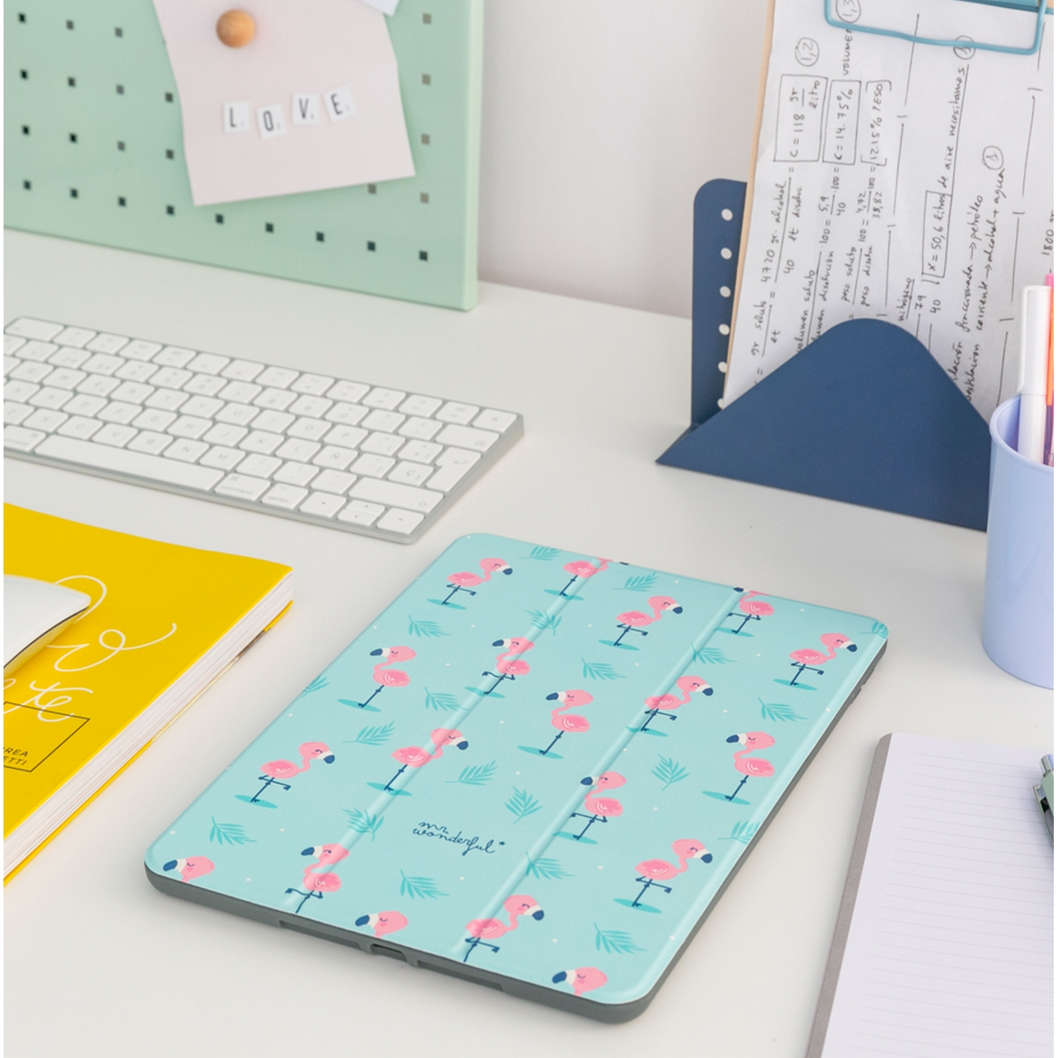 Una tableta con una funda con estampado de flamencos, sobre un escritorio con teclado y papelería.