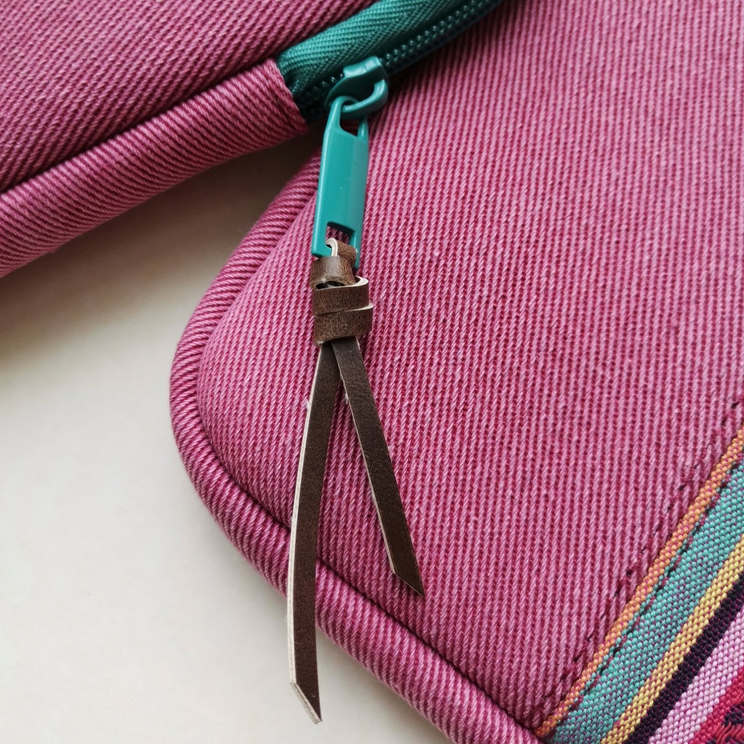 Primer plano de una bolsa rosa con cremallera y cremallera verde. Tiras de cuero marrón.