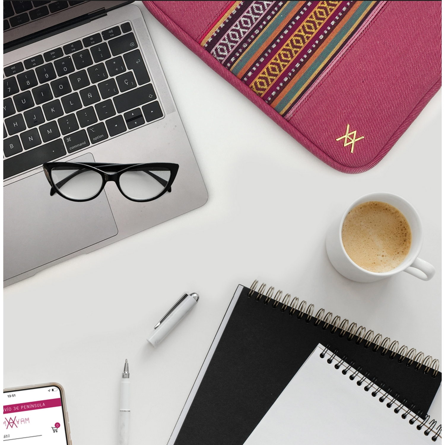 Vista cenital de un escritorio con un portátil, gafas, bolígrafo, bloc de notas y una taza de café.