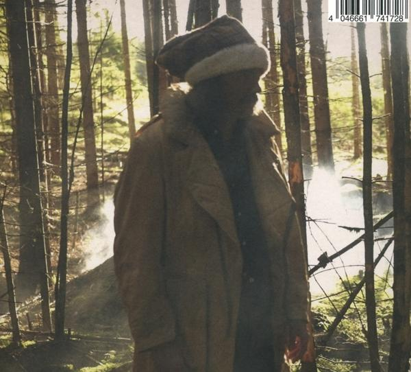 Ein Mann in Mantel und Hut geht durch einen Wald, Sonnenlicht durch Bäume.